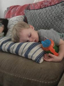 A young kid on a couch asleep with his fast resting on a striped pillow.