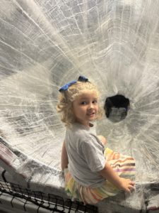 A girl sitting at the top of the packing tape slide at the Discovery Lab in Tulsa, one of Oklahoma best stem experiences!