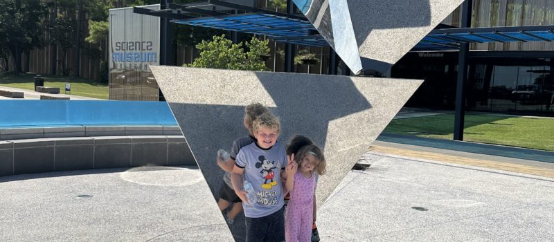 Two kids standing by the geometric sculpture, Finity, in front of Science Museum Oklahoma enjoying Oklahoma's STEM experiences.