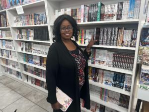 The author standing by the bookshelves in One Stop Anime showing ways to support small businesses